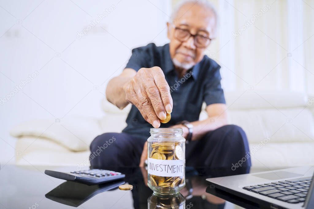 Senior man counting and savings coins in a jar with investment text on table. Finance and Investment concept