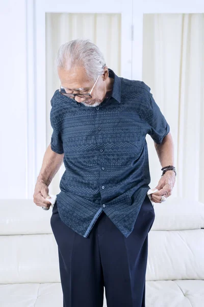 Preoccupato Uomo Anziano Mostrando Tasca Vuota Mentre Piedi Soggiorno Casa — Foto Stock