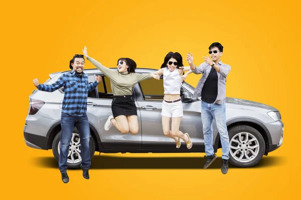 Sarı Arka Planı Olan Arabanın Yanında Birlikte Atlayan Neşeli Gençlerin — Stok fotoğraf