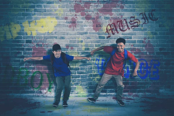 レンガの壁を背景にバックパックを持っている間二人の面白い大学生が一緒に愚かなダンスを行う — ストック写真