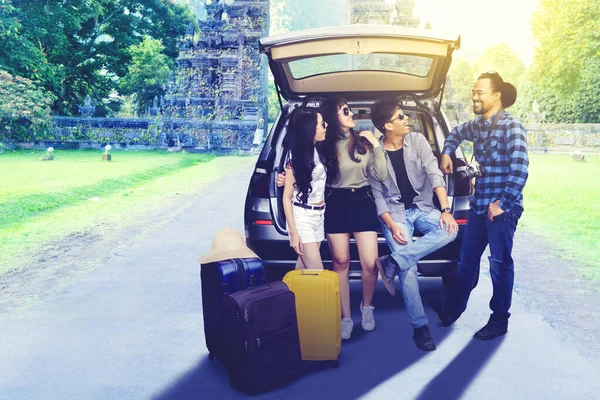 スーツケースを持って車の後ろに立っている間に一緒に笑っている若者の肖像グループ — ストック写真