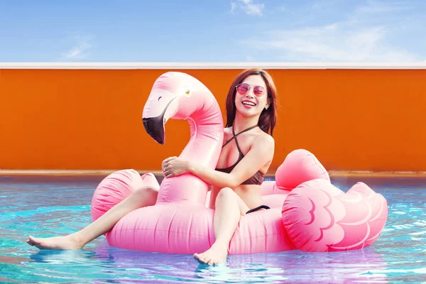 穿着比基尼的快乐的年轻女子坐在游泳池的充气火烈鸟上 — 图库照片