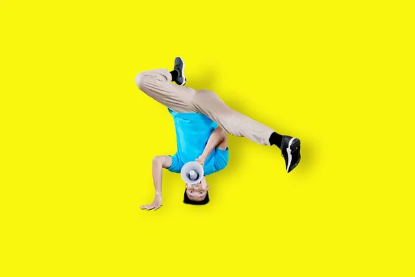 Young man dancing break dance while shouting with megaphone in the studio with yellow background