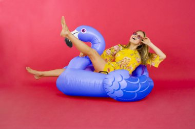 Stüdyoda kırmızı arka planda Flamingo üzerinde otururken eğlenen güzel bir kadının portresi 