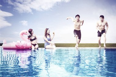 Güzel genç kadınlar erkek arkadaşlarının yüzme havuzuna atlamalarına bakıyor.