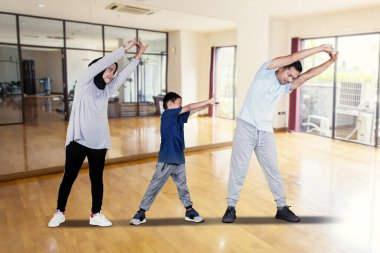 Genç bir aile spor salonunda dikilirken birlikte esneme hareketleri yapıyorlar. 