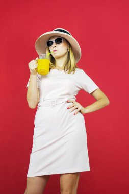 Stüdyoda eli belinde, kırmızı arka planda bir bardak meyve suyu içen genç kadının portresi. 