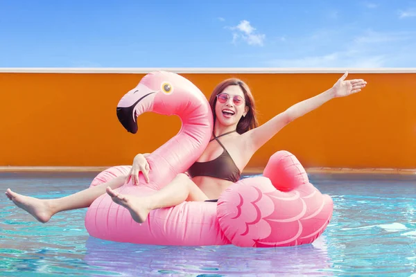 Pretty young woman in bikini sitting on the inflatable flamingo on the swimming pool