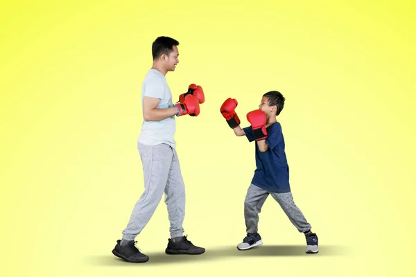 年轻父亲和小男孩戴着拳击手套和黄色屏风进行拳击运动的画像 — 图库照片