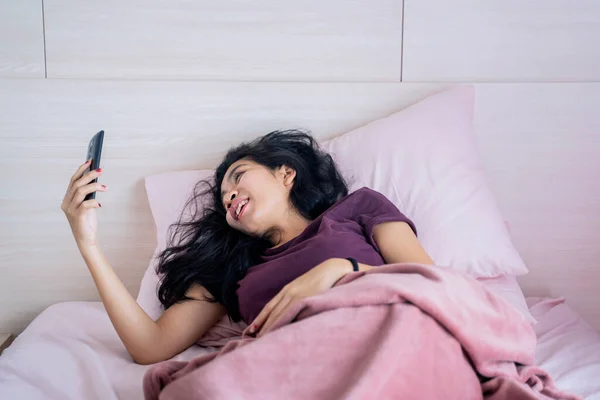 Portret Azjatki Uśmiechającej Się Patrzącej Komórkę Podczas Leżenia Samoizolacji Łóżku — Zdjęcie stockowe