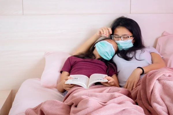 小女儿和她的母亲头戴面具 拿着一本书睡在床上的画像 — 图库照片