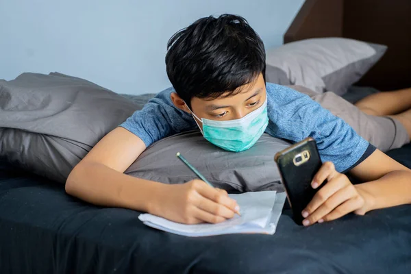 男同学在家用智能手机学习 同时在卧室戴医疗面具的肖像 — 图库照片