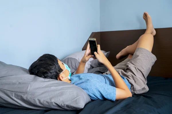 ベッドの上に横たわっている間 彼のスマートフォン上の小さな男の子の読書メッセージの写真 社会的距離の概念 — ストック写真