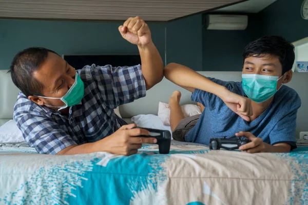 Portrait of son and father playing video game while wearing medical mask and doing social distancing at home
