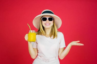 Stüdyoda kırmızı ekranlı kameraya gülümserken elinde bir bardak portakal suyu tutan neşeli kadının portresi. 