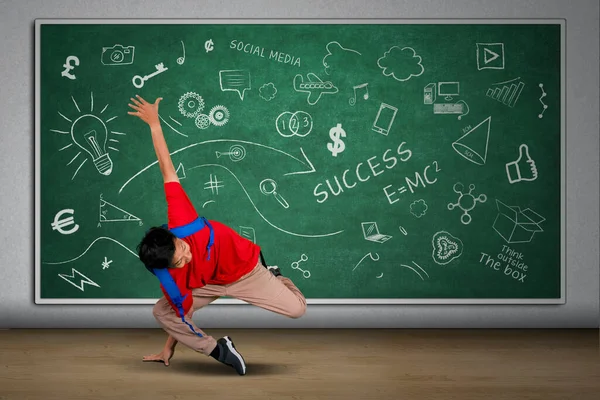 Picture of university student doing handstand in the classroom while carrying backpack with doodles on the blackboard