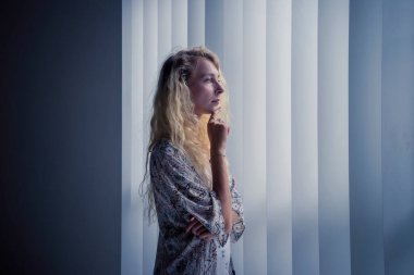 Pencere önünde durup çenesini tutarak hayal kuran düşünceli bir kadın.