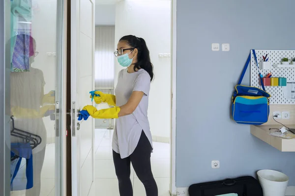 亚洲女人站在卧室里用消毒剂擦拭门把手的肖像 — 图库照片