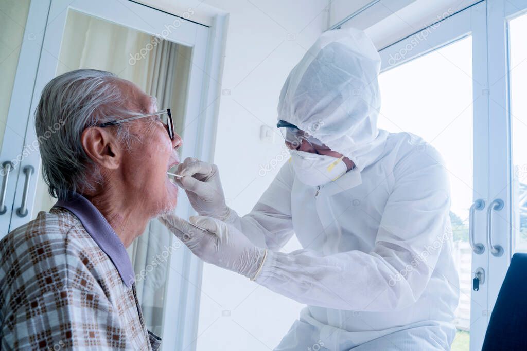 Portrait of unidentified doctor wearing hazmat suit and face mask while checking up his old Asian patient's mouth in the hospital