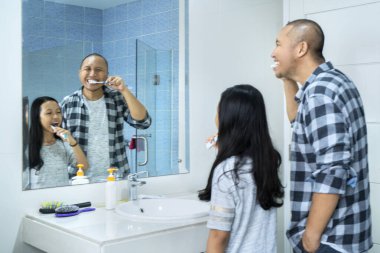 Küçük kız ve babası aynanın önünde dikilirken banyoda dişlerini fırçalıyorlar. Evde vuruldu.