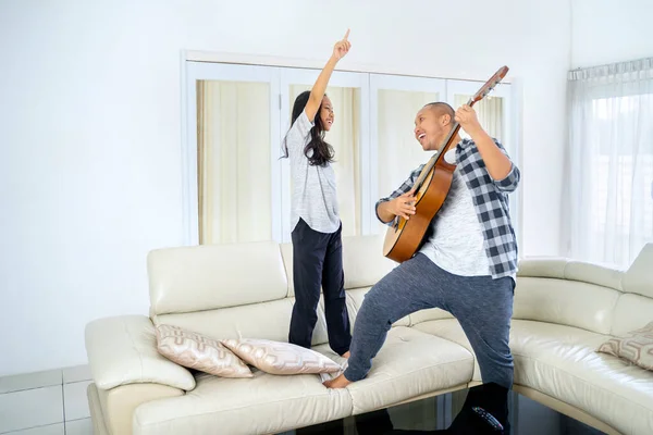 若い男がギターを演奏し 自宅のリビングルームで娘と一緒に踊ります 4Kの解像度で撮影 — ストック写真