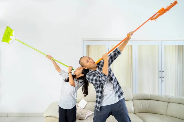 年轻人和他的女儿在客厅里一起玩的时候 用扫帚和拖把当喇叭 在家里中弹 — 图库照片