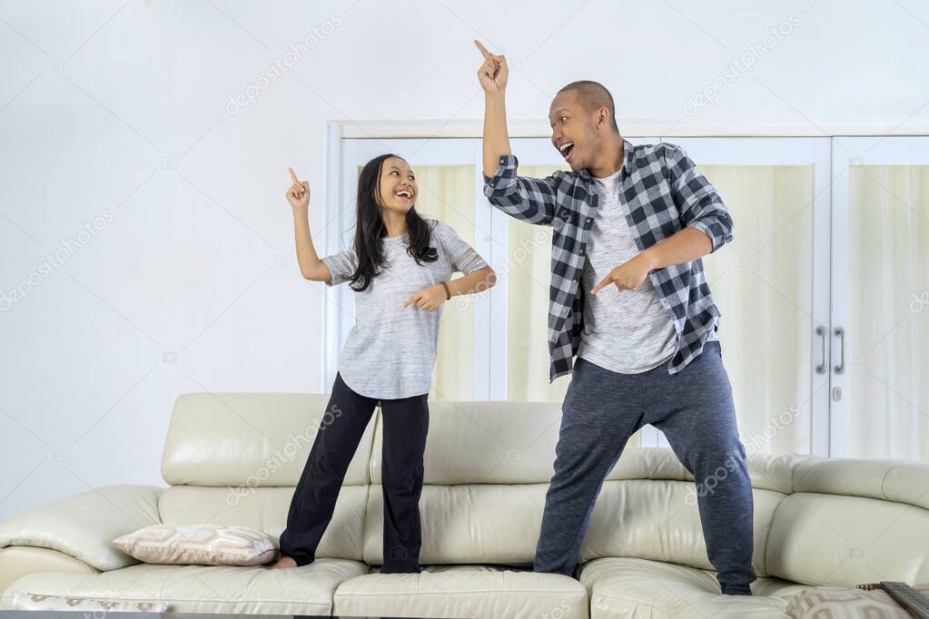 Young father and his daughter dancing together while standing on the couch at home. Shot in the living room