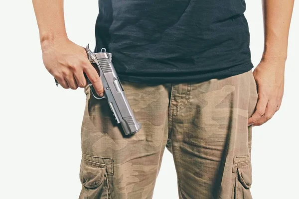 Un hombre sosteniendo un arma. Hombre en pantalones de camuflaje sosteniendo un arma aislada sobre fondo blanco, Ejército, pistola semiautomática, 45 pistolas — Foto de Stock