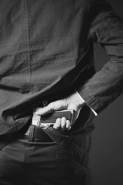 Um homem, policial ou gangster escondendo sua arma nas costas — Fotografia de Stock