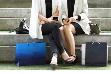 Açık havada alışveriş torbaları ile oturan ve kullanarak kadın akıllı telefonlar, yaşam biçimi, alışveriş, teknoloji ve dostluk ile ilgili kavramlar.