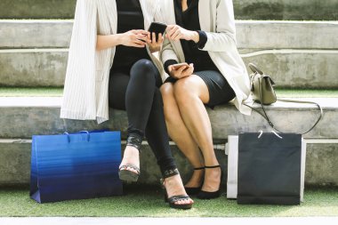 Açık havada alışveriş torbaları ile oturan ve kullanarak kadın akıllı telefonlar, yaşam biçimi, alışveriş, teknoloji ve dostluk ile ilgili kavramlar.