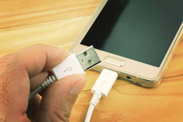 Cabo USB com telefone inteligente na mesa de madeira . — Fotografia de Stock