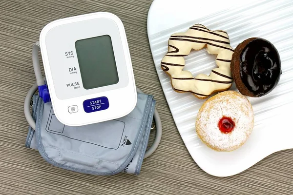 Digitales Blutdruckmessgerät und Donut, ungesunde Lebensmittel, Süßwaren. hoher Zucker. — Stockfoto