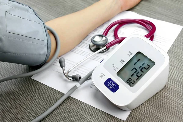 Läkare mäta blodtryck av patient, digitala blodtrycksmätare på trä bakgrund, medicinska prövningen utrustning. — Stockfoto