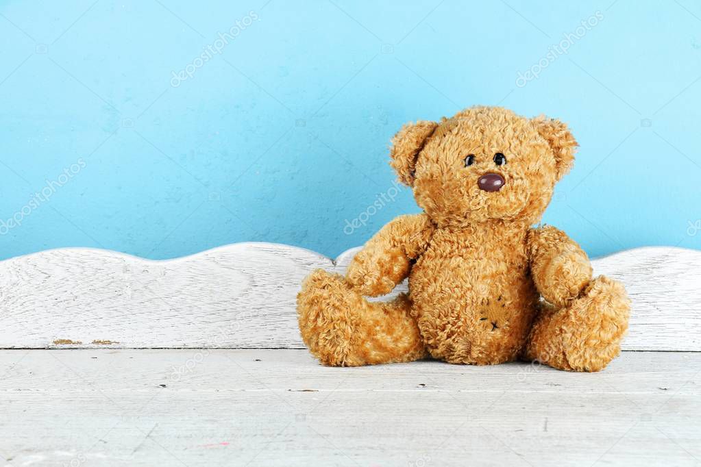 Teddy Bear toy alone on white wooden table in front of blue background.
