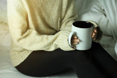 Bir fincan sıcak içecekler, kış sabahı evde yatakta, duygu sıcak kavramı tutan bir rahat kazaklı kadın.