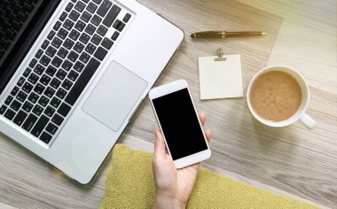 Bir fincan kahve ile ahşap zemin üzerinde smartphone ve dizüstü bilgisayar kullanarak, evde kavramı çalışan kadın.