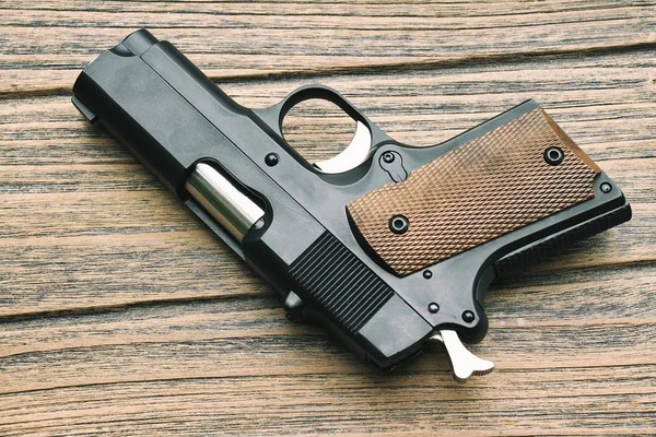 Primer plano de la pequeña pistola negra (pistola compacta) acostada sobre fondo de madera, pistola .45, pistola de mujer . — Foto de Stock