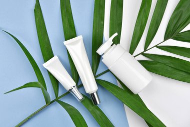 Kozmetik şişe kapları ile yeşil bitki yaprakları, boş etiket markalama mock-up, doğal güzellik ürün kavramı, için düz renk arka plan üzerinde yatıyordu..