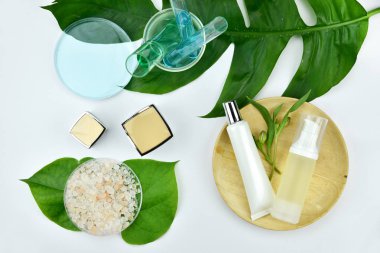 Kozmetik şişe kapları ile yeşil bitki yaprakları.