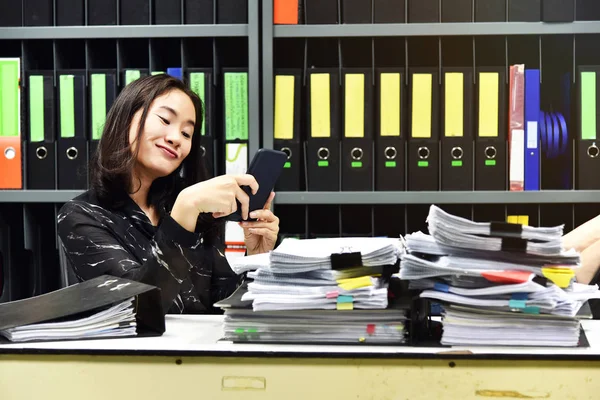 Лінива азіатська офісна жінка використовує мобільний смартфон у робочий час, не продуктивний працівник . — стокове фото