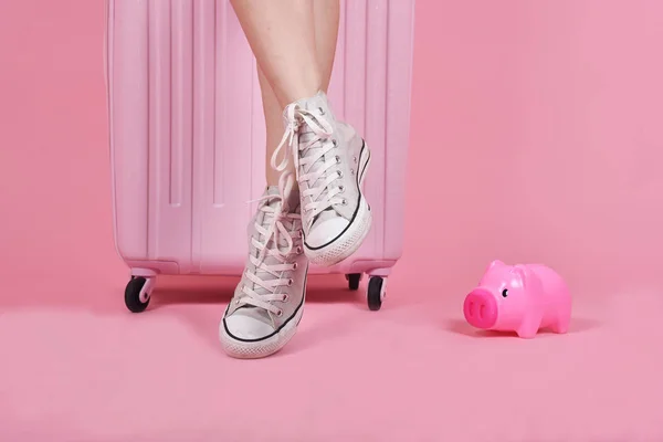 Young woman traveler sitting on suitcase over pink background, Journey and travel concept.