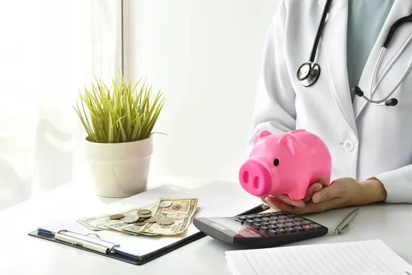 Medical and health insurance concept, Doctor holding piggy bank and money in hospital background, Money saving for medical care expenses.