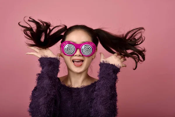 Joyeuse femme asiatique, Fille excitée portant des lunettes drôles sur fond rose isolé, Fille gaie sautant avec le visage de bonheur . — Photo