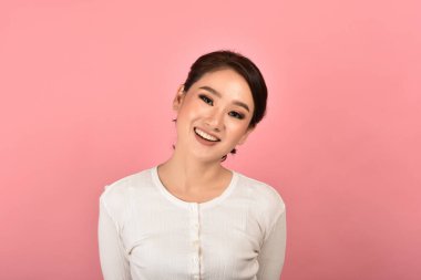 Pembe arka planda dinlenen Asyalı kadın, mutlu orta yaşlı kadın portresi günlük giysiler içinde kameraya bakıyor..