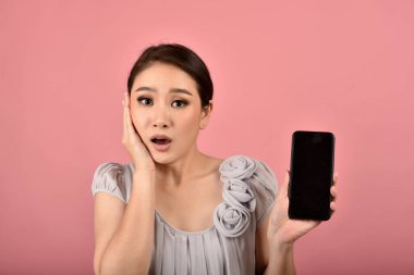 Şüpheli ve sorgulayıcı yüz ifadesine sahip Asyalı kadın elinde akıllı telefon, sahte haber ve internet sosyal medyası aracılığıyla yayılan sahte yanlış bilgi tutuyor..