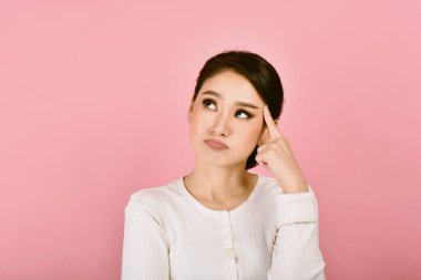 Düşünceli, kafası karışmış ve başı dönen Asyalı kadın, kızın yüz ifadesi endişeli, pembe arka planda karışık sorunlar yaşıyor..