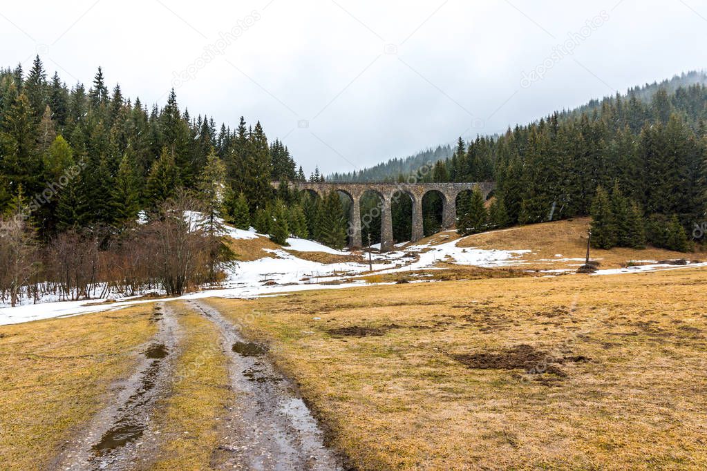 Slovakia train viaduct historical bridge in the forest and mountains. Historic railroad and transportation. Meadow with snow in foreground, snowy winter weather