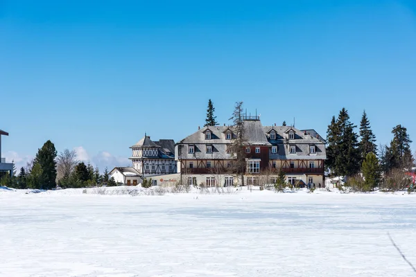 Slowakei: strbske pleso resort, Blick auf den zugefrorenen See im Winter und Hotelresort darüber. blauer Himmel. — Stockfoto