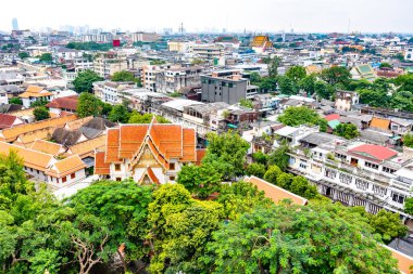 Tayland 'ın Bangkok şehrinin Panorama manzarası. Şehirdeki yerleşim yerleri ön planda, tapınaklar, gökdelenler ve modern binalar. Taze ağaçlar ve bitkiler. Bulutlu hava, dramatik bulutlar.